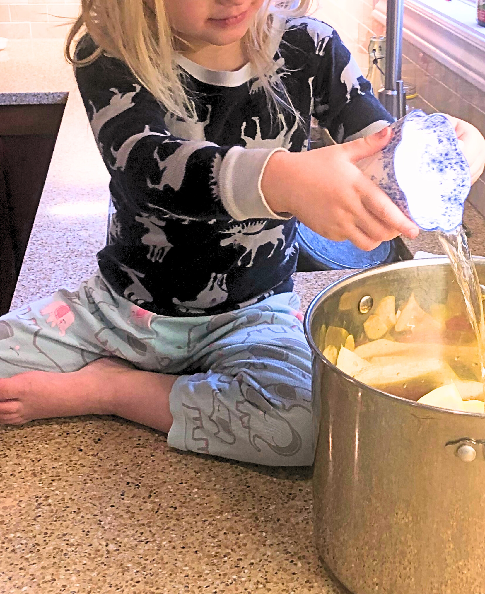 A little girl pouring water into a pot of apples.