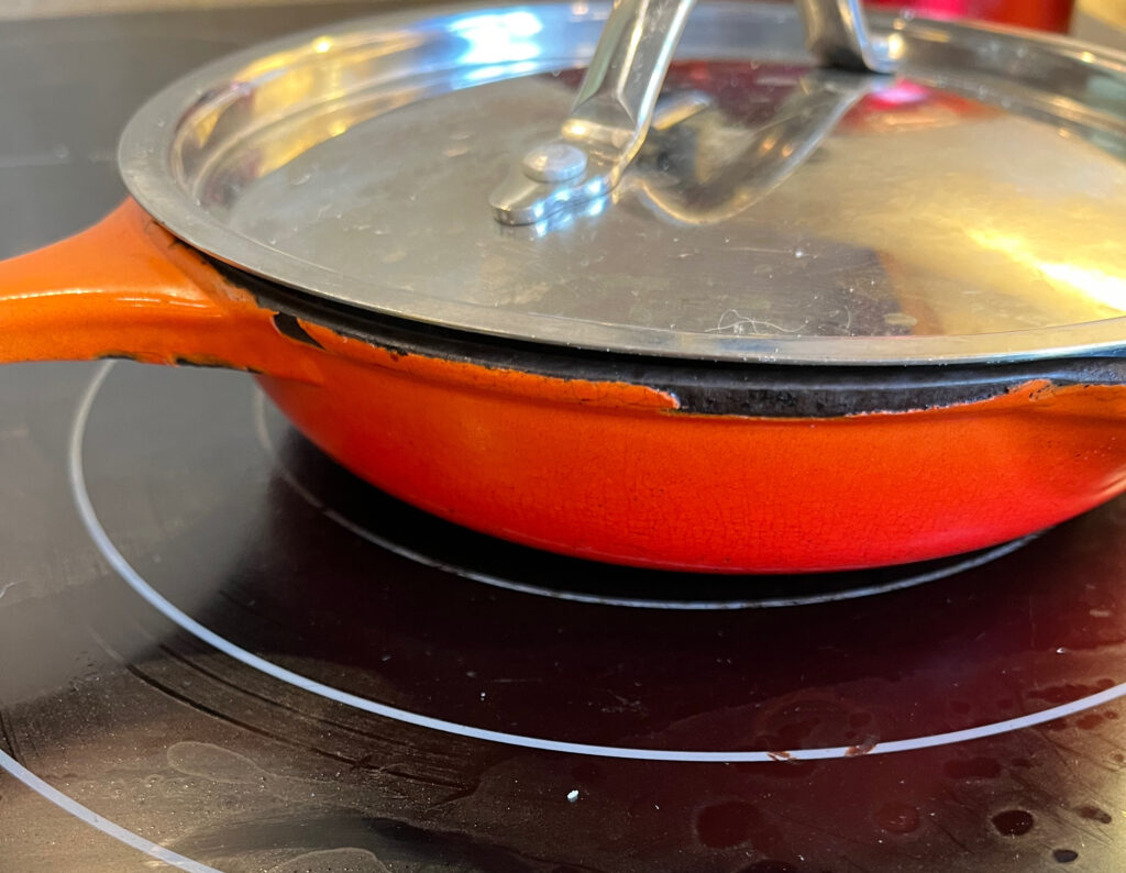 An orange pan with a metal lid on a black stove top.