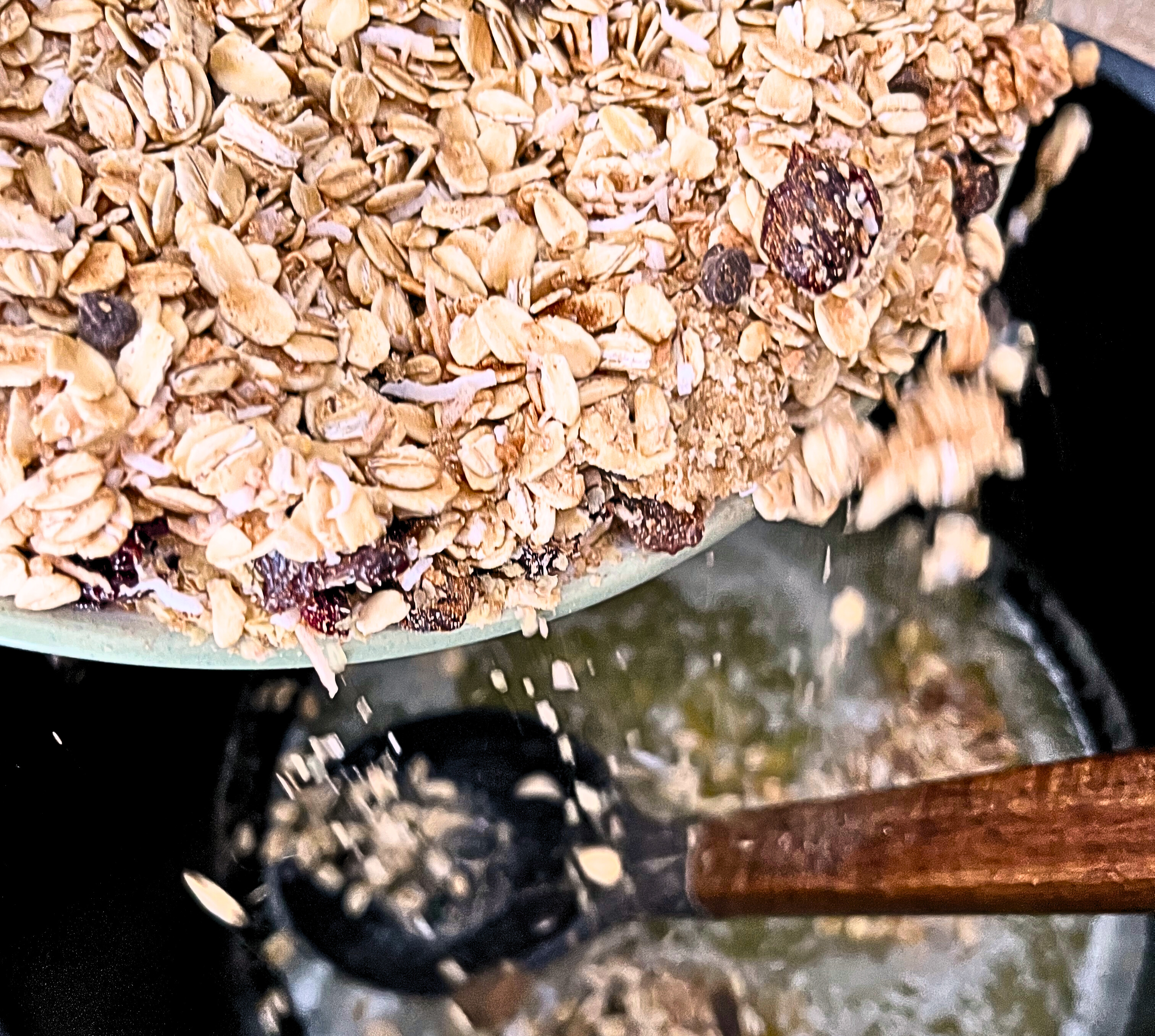 Pouring a bowl of dry granola ingredients into a pot of melted butter and honey.