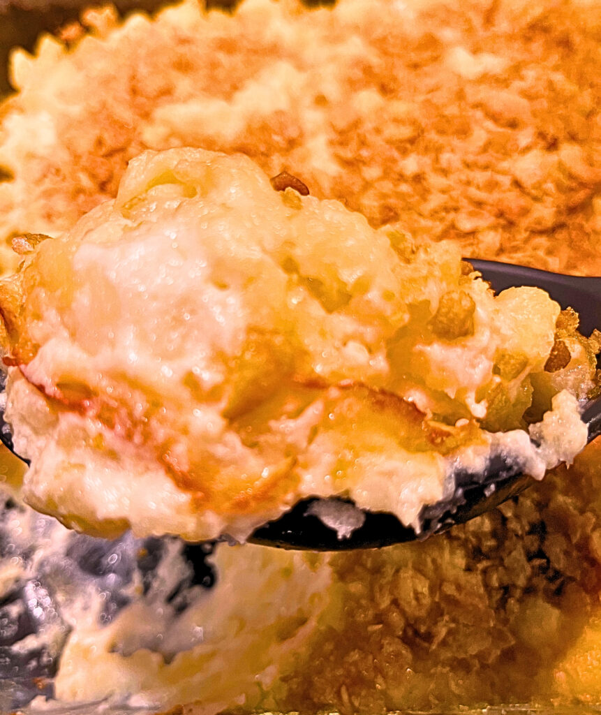 A large black spoon holding In a hurry scalloped potatoes, with a casserole dish in the background.
