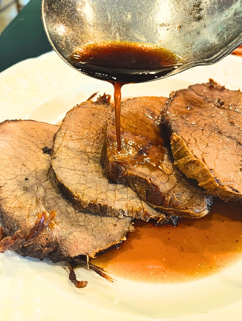 The best overnight beef pot roast on a white plate with a silver spoon pouring over the au jus.