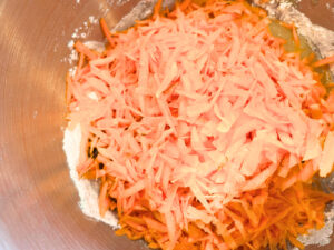 A mixing bowl with batter and shredded carrot on top.