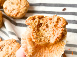 A woman holding up a carrot muffin with a bite out of it.