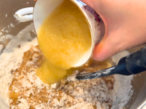 A woman pouring apple sauce into a mixing bowl with batter.