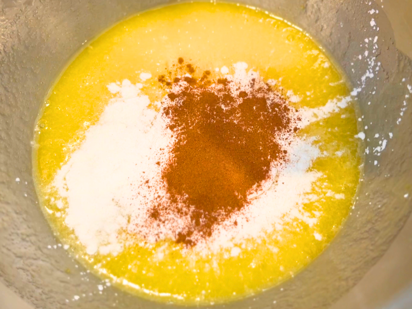 A mixing bowl with a yellow liquid, white powder, and brown powder inside.