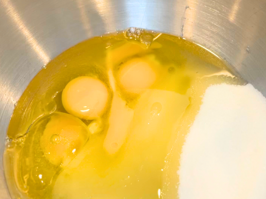 A mixing bowl with eggs, sugar, and oil.