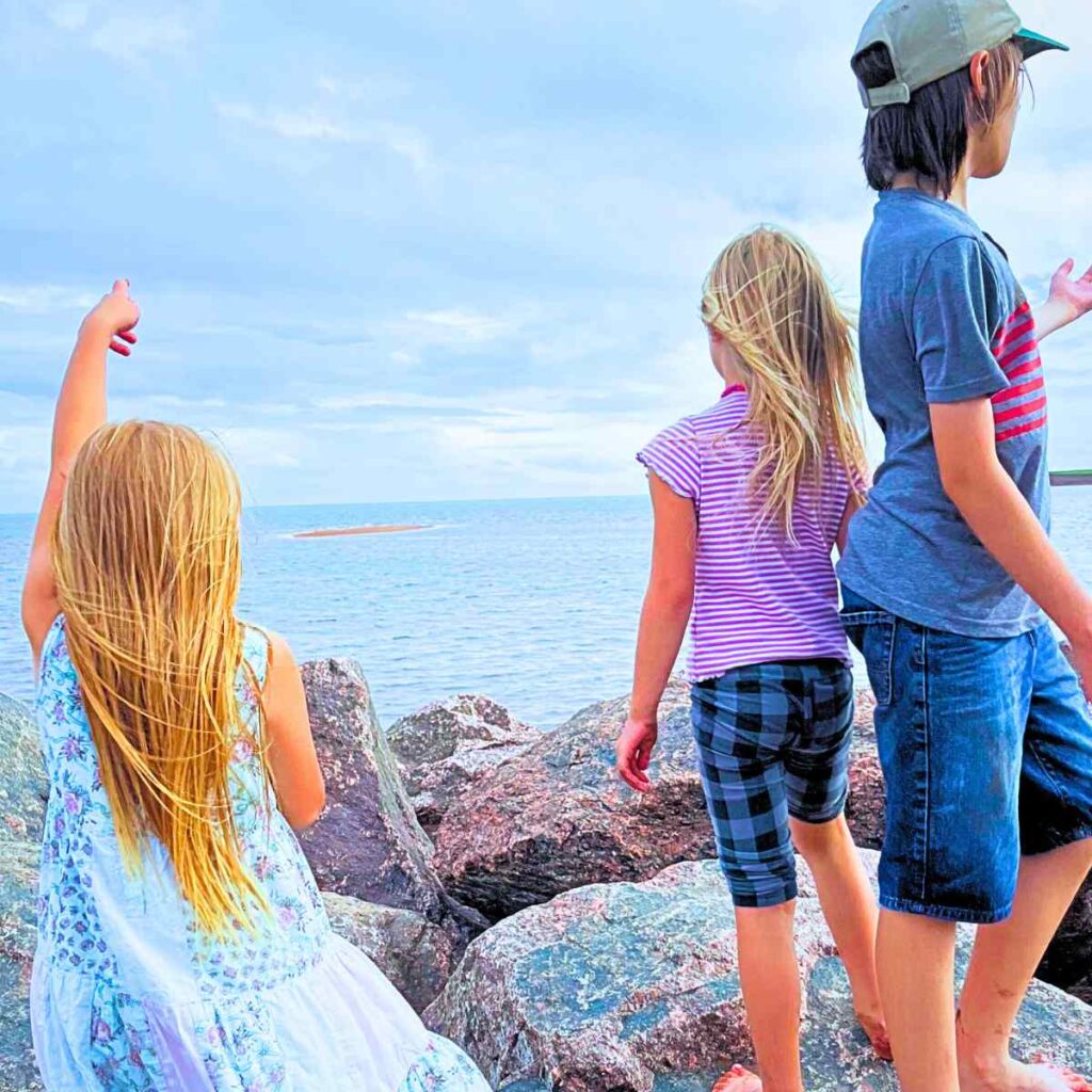 Three kids standing on rocks looking out over the ocean.