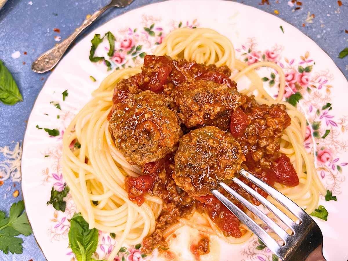 There is a plate of spaghetti and meatballs. A woman is sticking a fork in one of the meatballs.