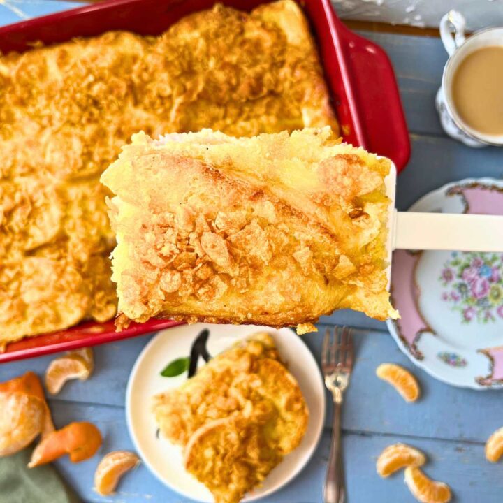 There is a breakfast casserole in a red dish. A woman is holding a serving of the casserole on a white spatula.