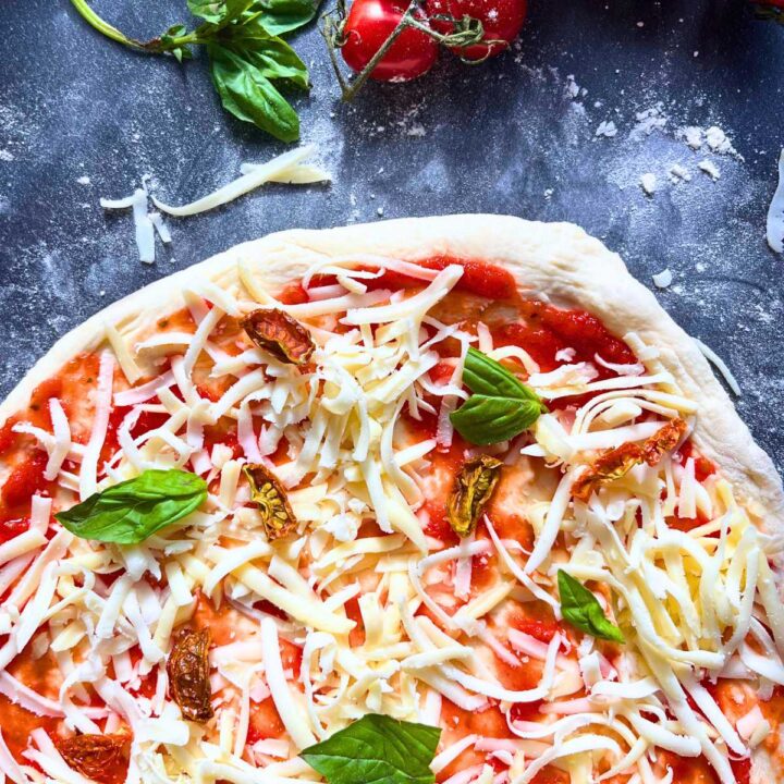 An overhead look of an unbaked pizza with cheese, basil, and sun dried tomatoes on top.