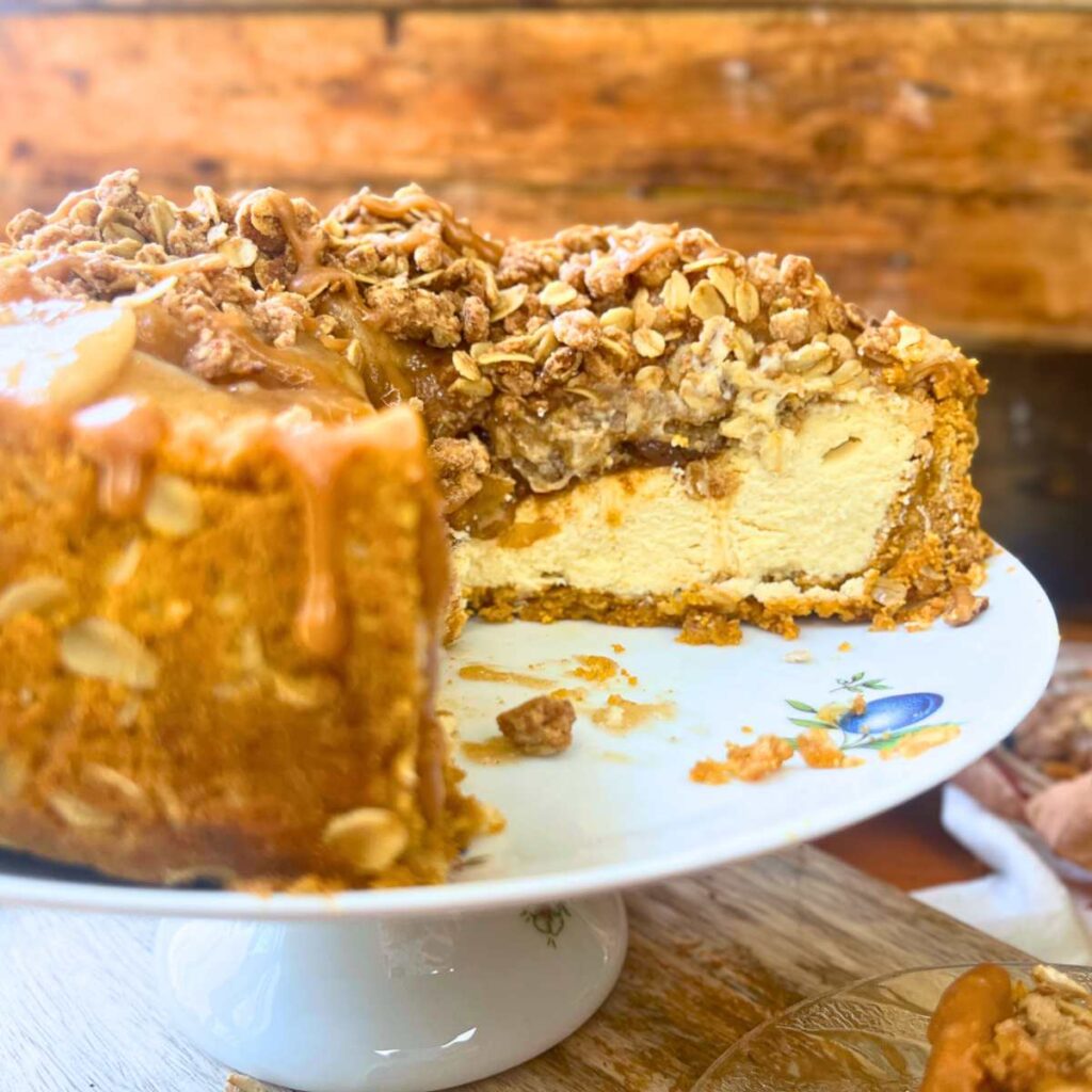 A side view of a sliced apple crisp cheesecake on a cake stand.