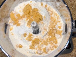 A food processor with flour and brown sugar inside.