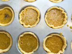 Unbaked butter tarts in a muffin tray.