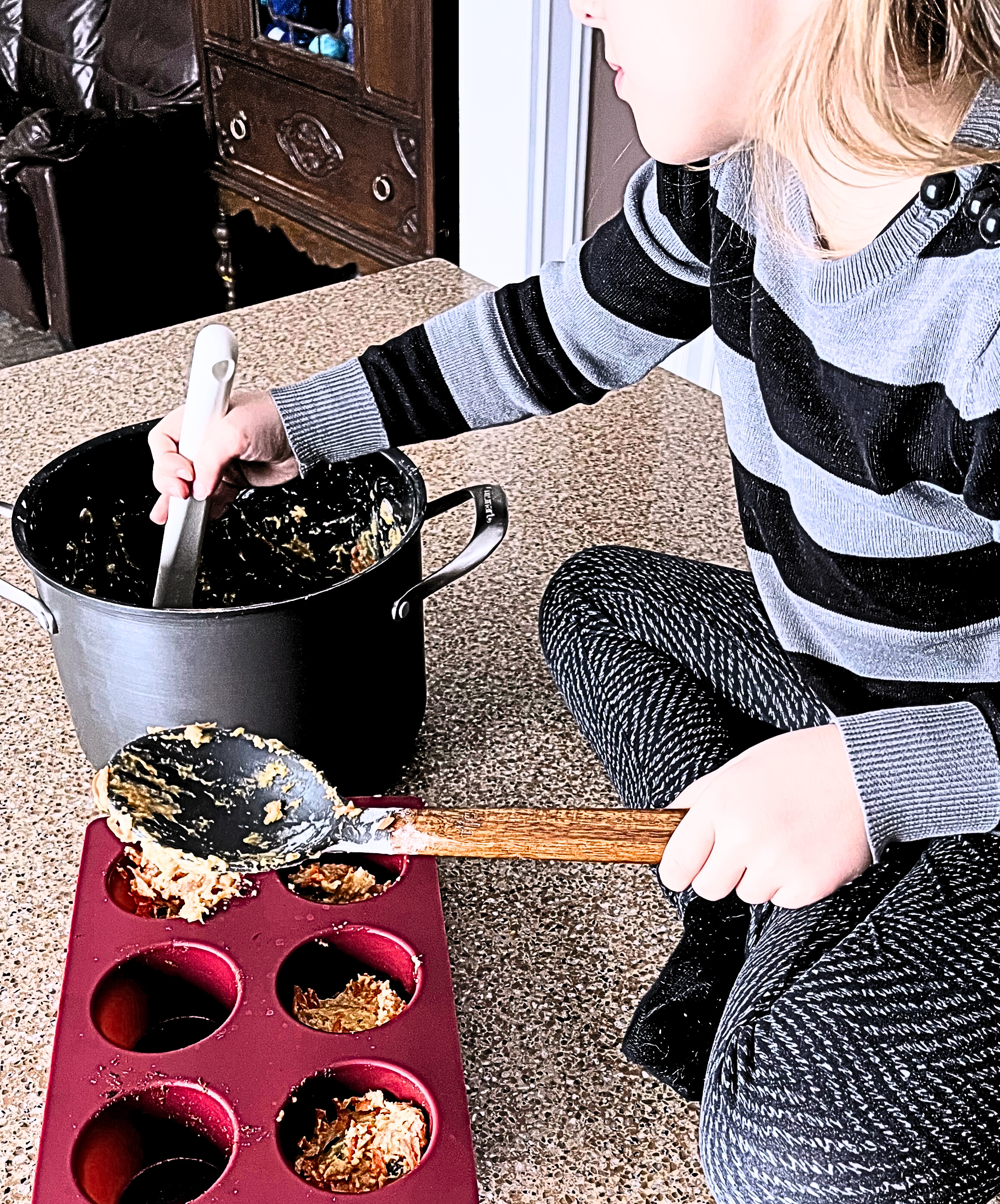 A little girl scooping muffin batter into a muffin tray.