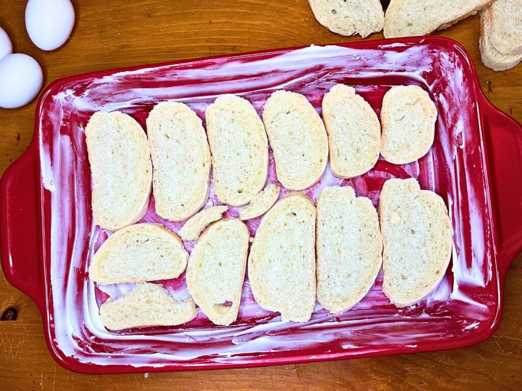 A red casserole dish with sliced bread in the bottom.