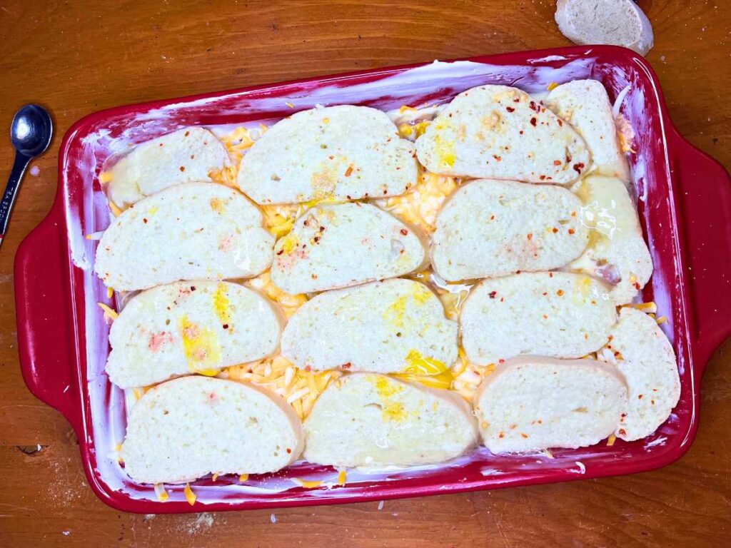 A red casserole dish with an uncooked breakfast casserole inside.