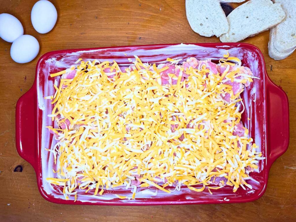 A red casserole dish with bread, peameal bacon, and grated cheese on top.