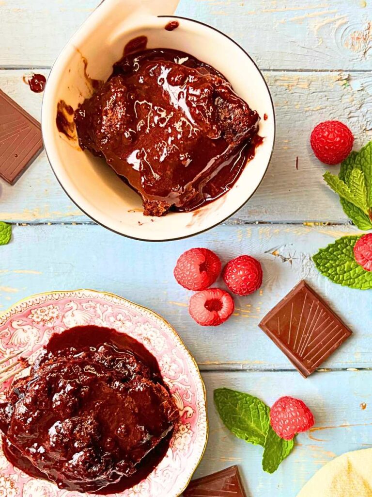 Two servings of chocolate pudding cake surrounded by raspberries and mint leaves.