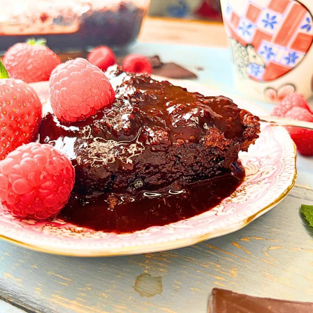 A chocolate cake with fudge sauce. There are raspberries on top.