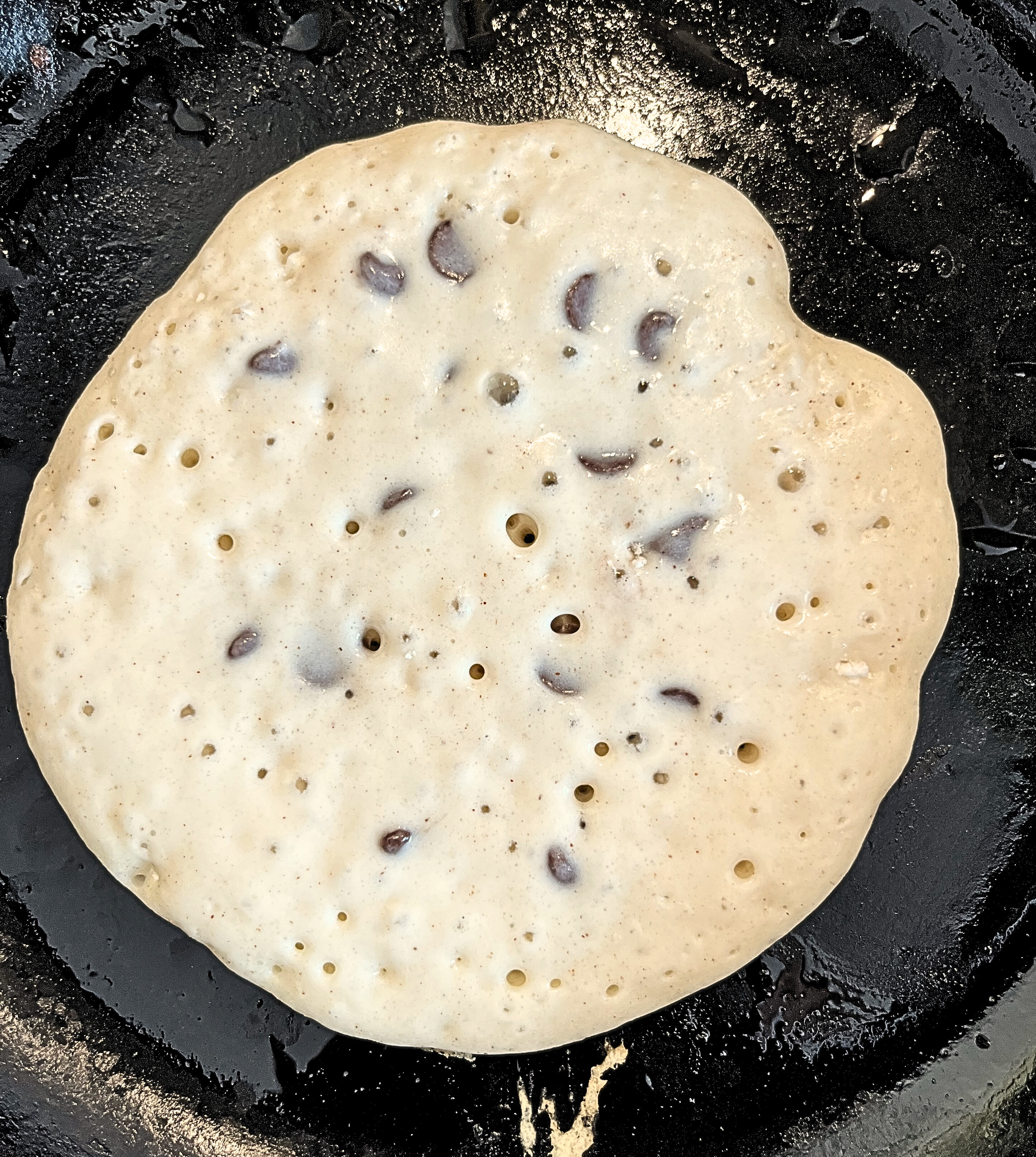 Cooking pancake batter with chocolate chips in it on a cast iron pan.