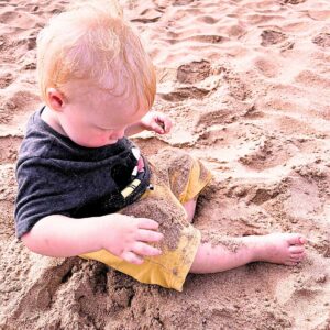 A toddler sitting in the sand.
