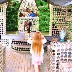 A girl walking in a church made from recycled bottles. There is a boy at the front of the church.