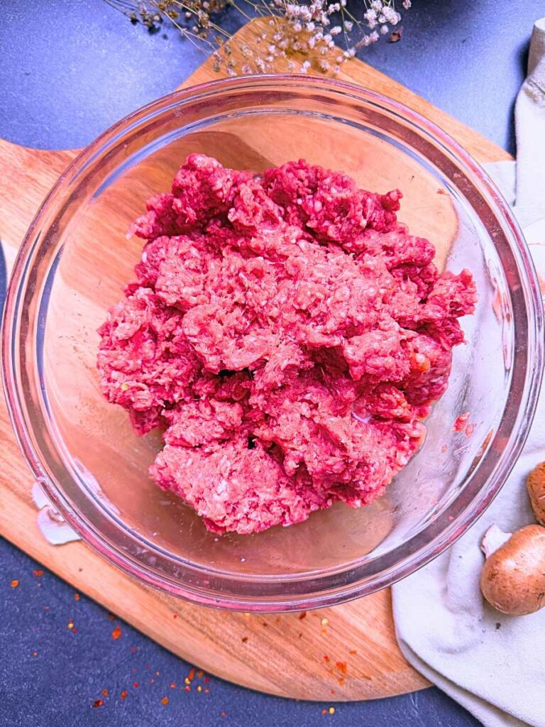 A glass bowl with ground beef inside.