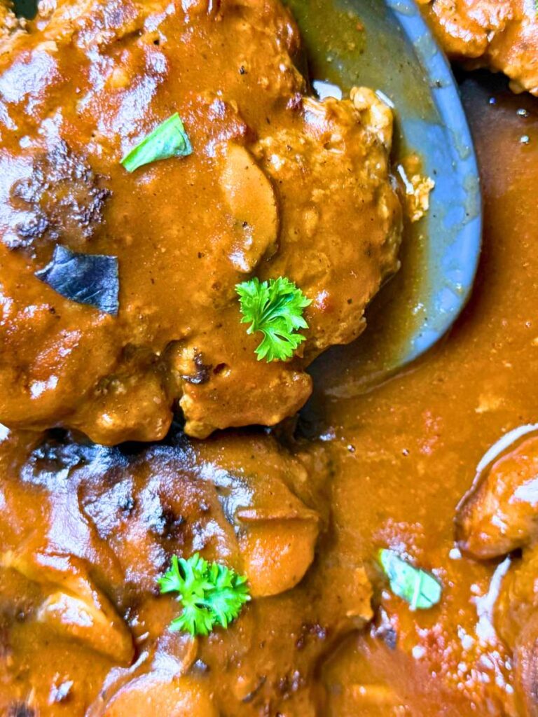 A close up view of a sauce pot filled with salisbury steaks and mushroom gravy.