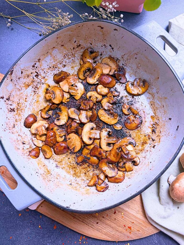 A Dutch oven with cooked, sliced mushrooms inside.