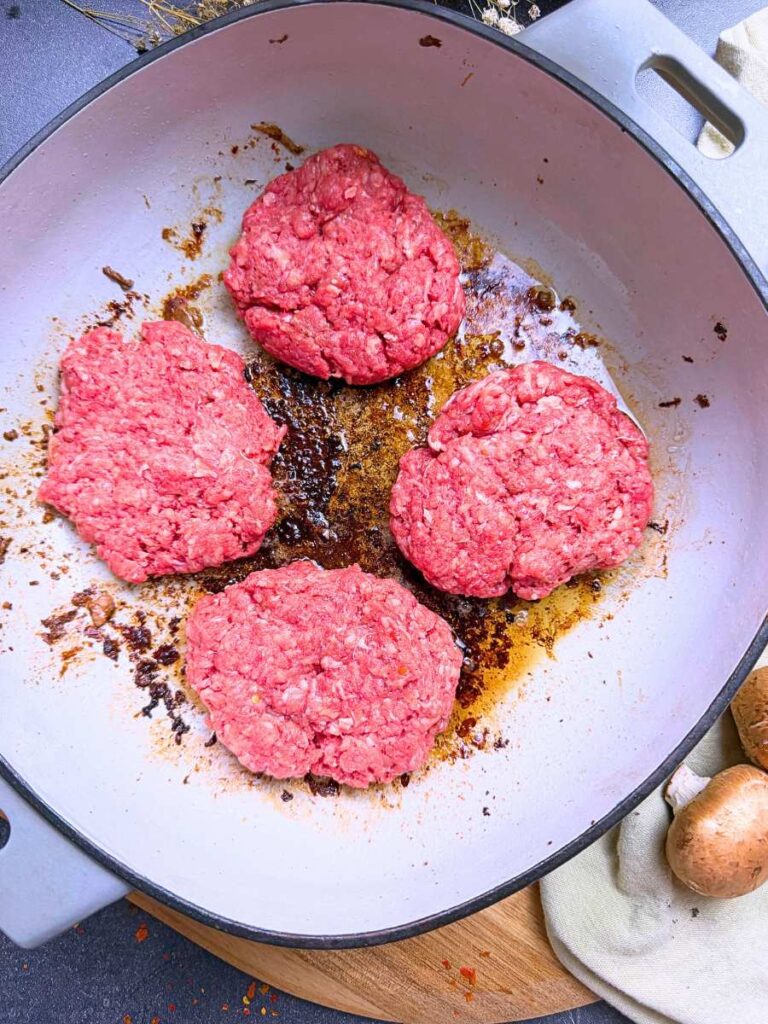 Four ground beef patties in a Dutch oven.