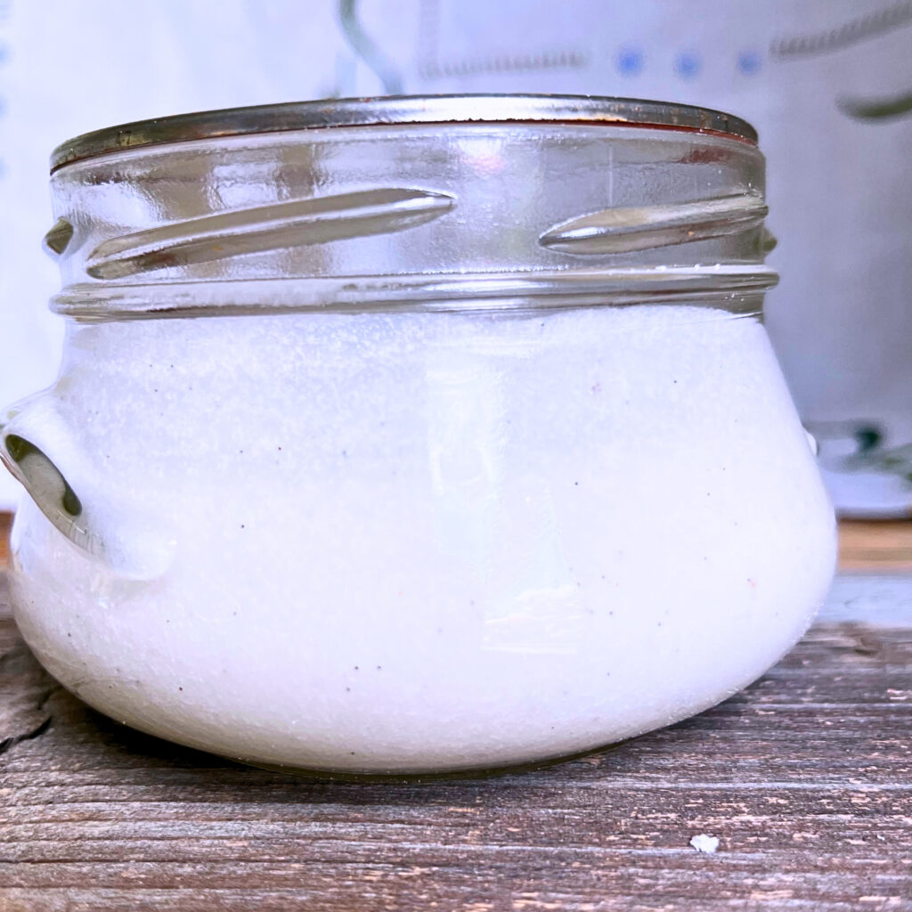 A jar of vanilla bean glaze on a wooden table.
