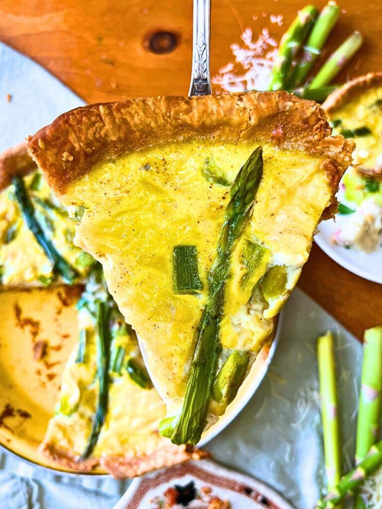 A woman is holding a slice of asparagus and Swiss quiche.