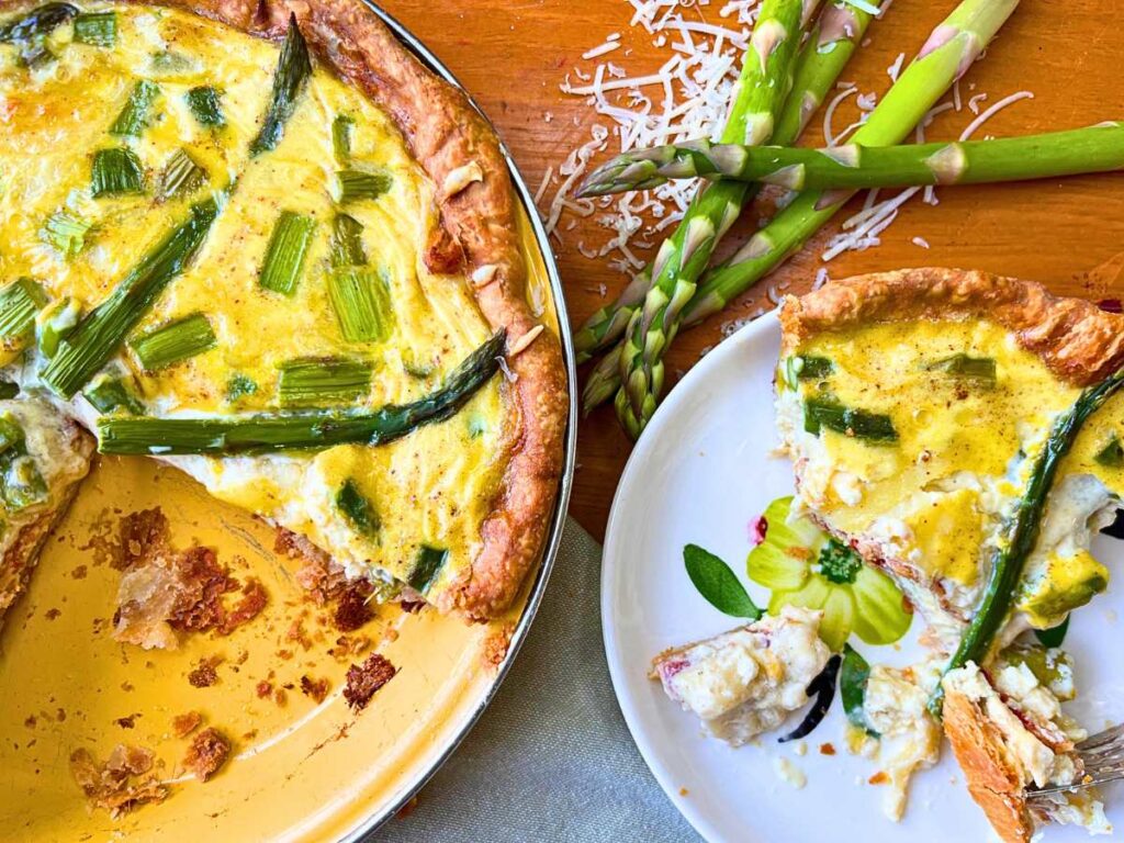 A sliced asparagus and Swiss quiche. There is a plate with a slice of quiche off to the side.