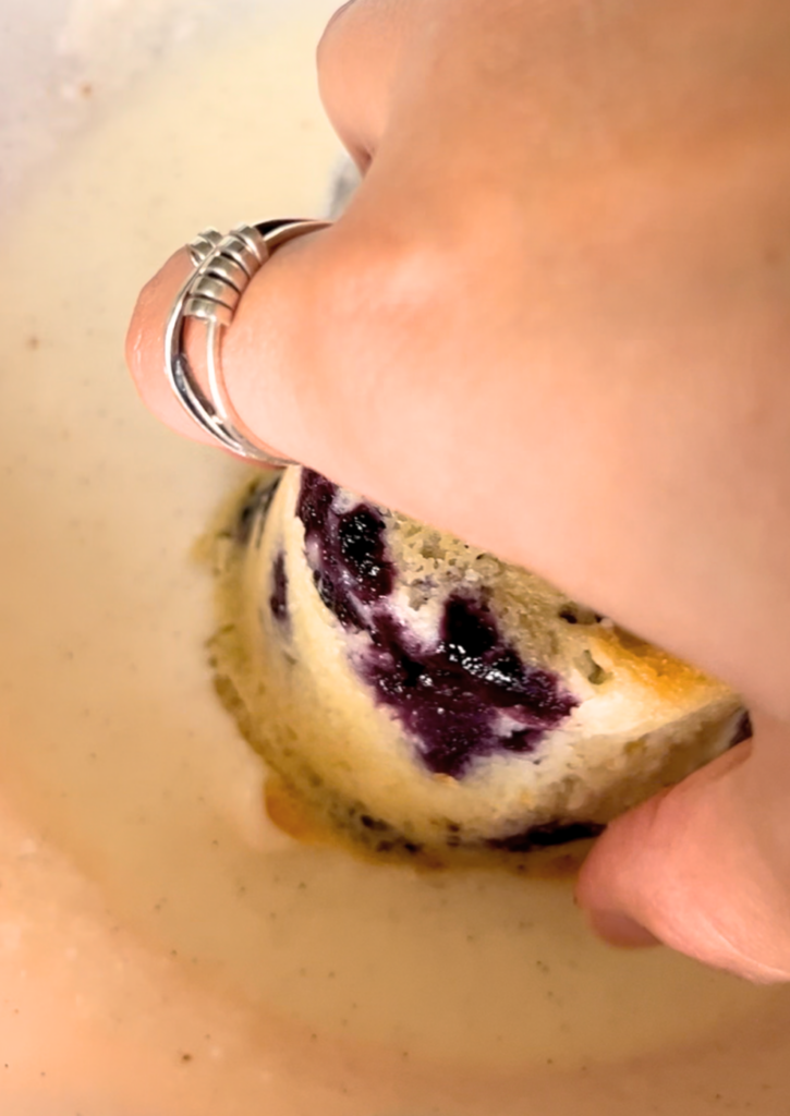 A woman dipping the top of a lemon blueberry muffin into vanilla glaze