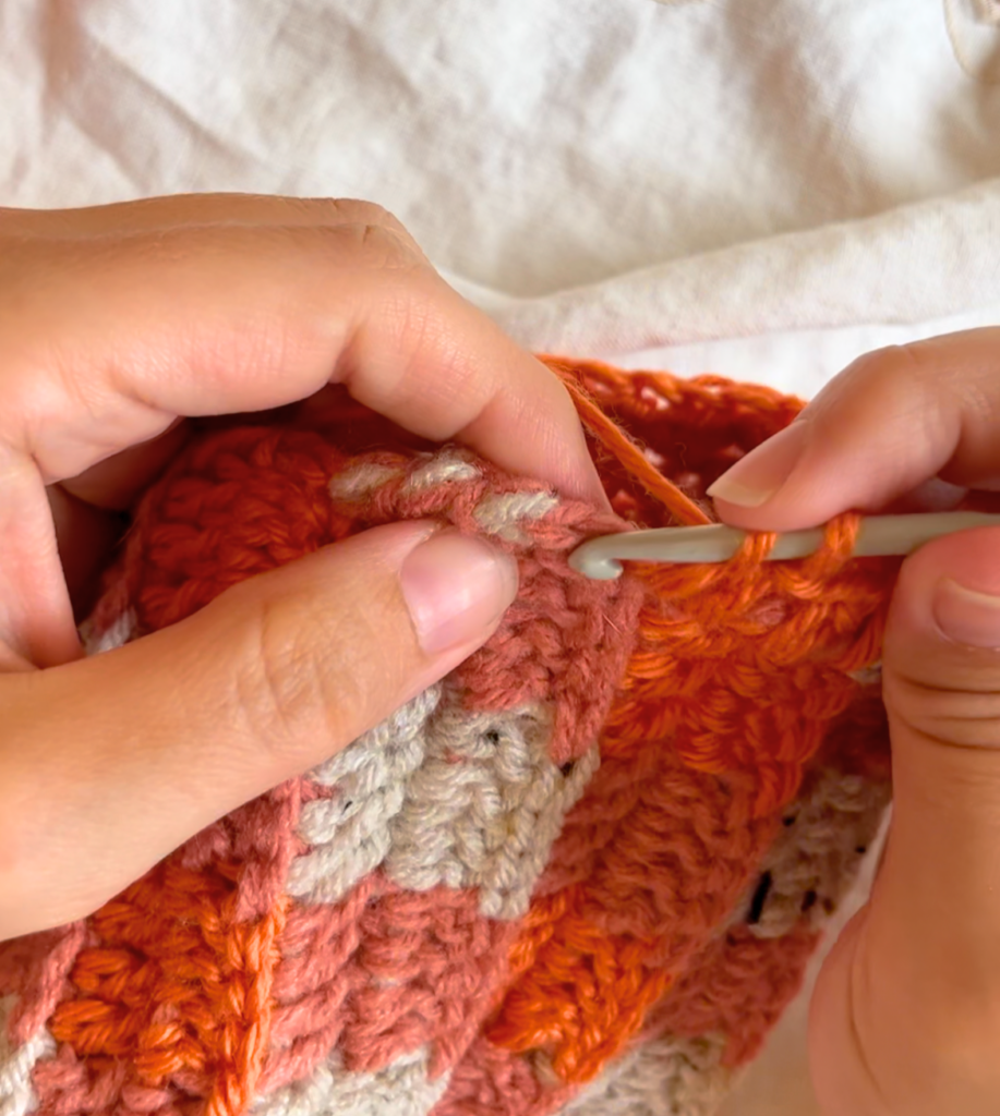 Using orange yarn to half double crochet a border around the bottom of an orange and grey buffalo plaid hat