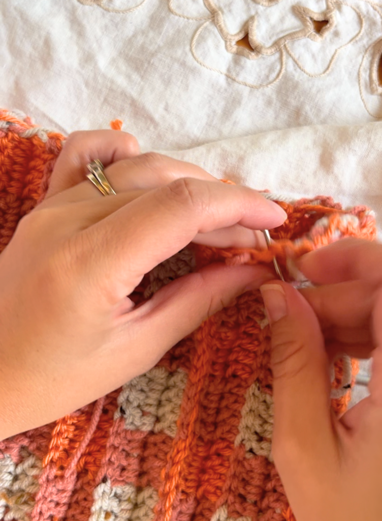 Woman sewing the top of an orange double crochet hat