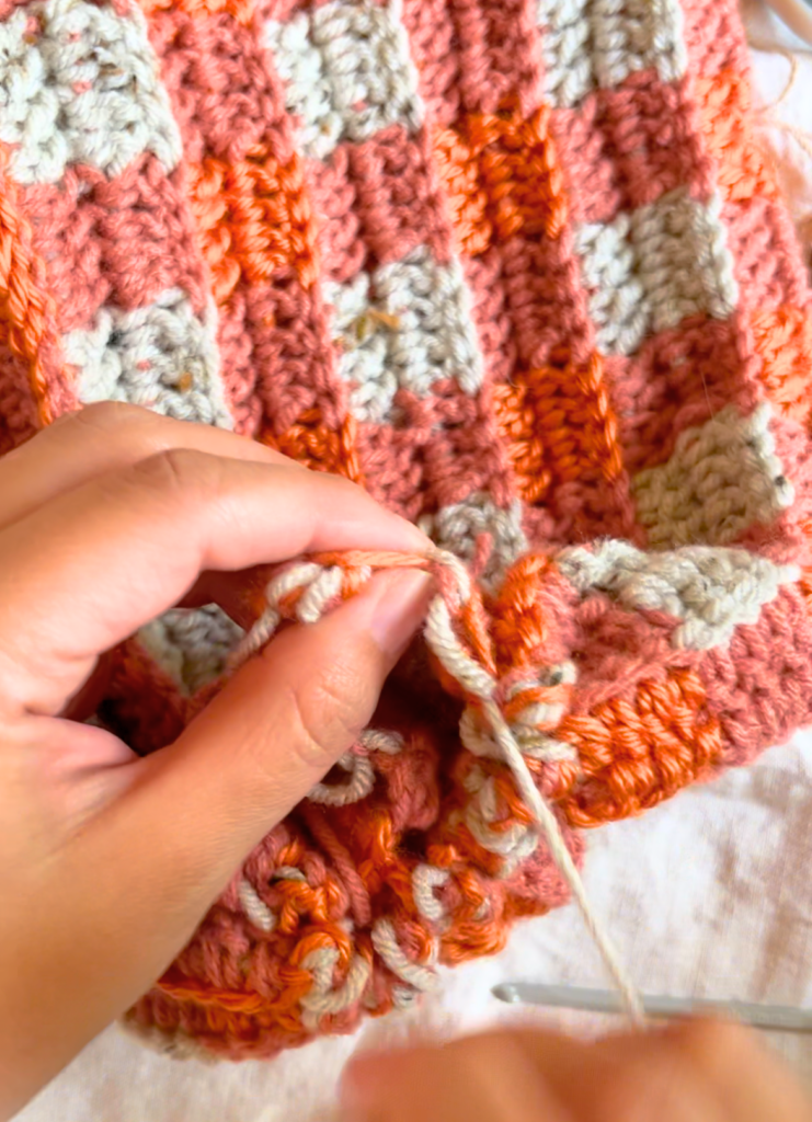 woman sewing the top of an orange double crochet hat