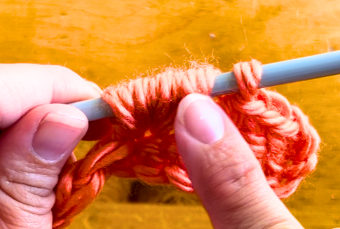 Orange yarn on a crochet hook. Puff stitch