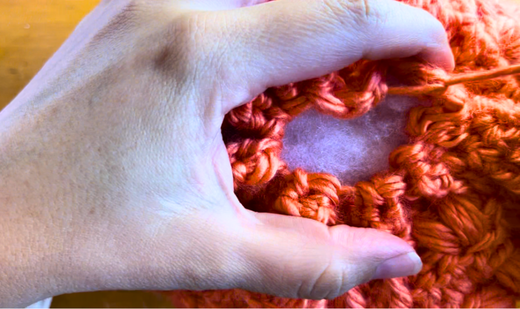 orange crochet pumpkin being stitched closed
