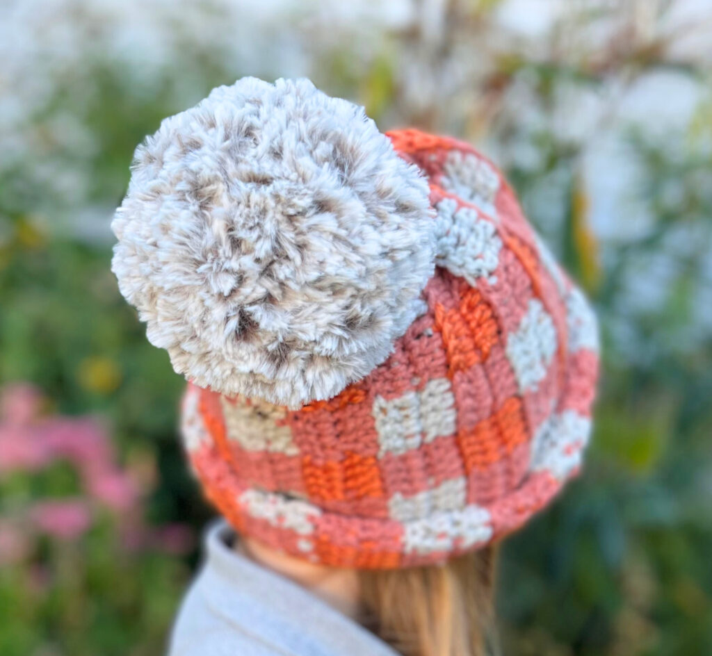 girl wearing an orange and white crochet hat with a large faux fur pompom