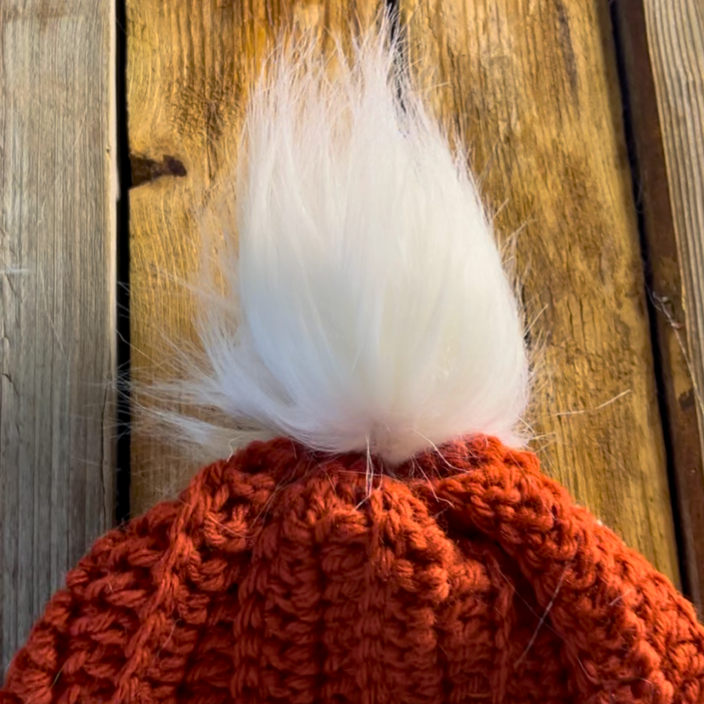 white faux fur material pompom on an orange crochet hat