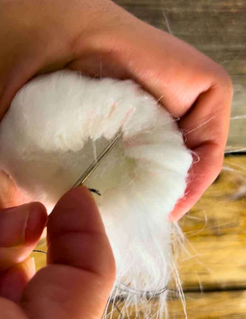sewing the top of white faux fur material to make a pompom