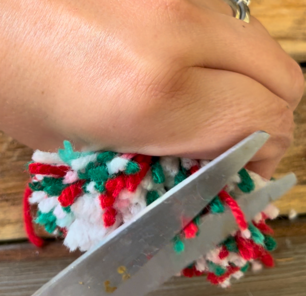 trimming red, white, and green yarn on a pompom