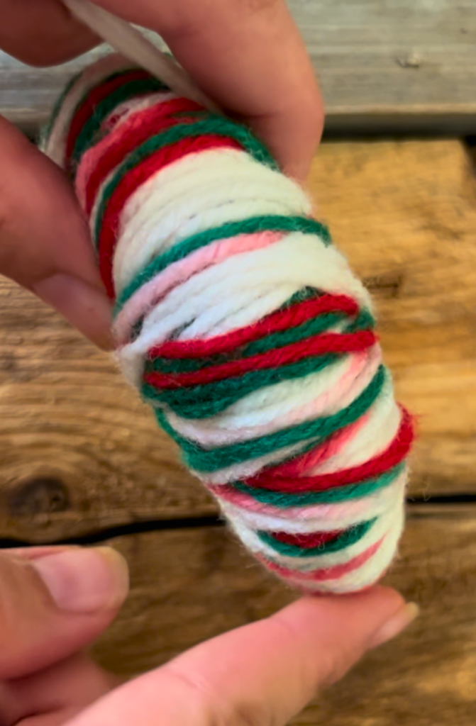 white, red, and green yarn wrapped around a piece of cardboard