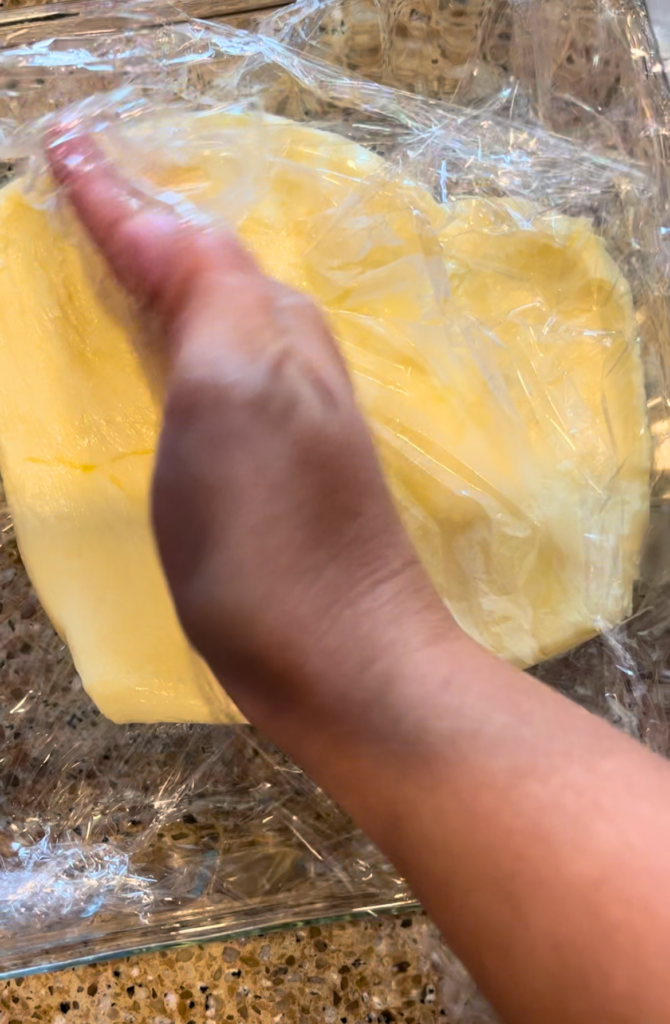 butter in a square glass pan being spread out by a woman's hand
