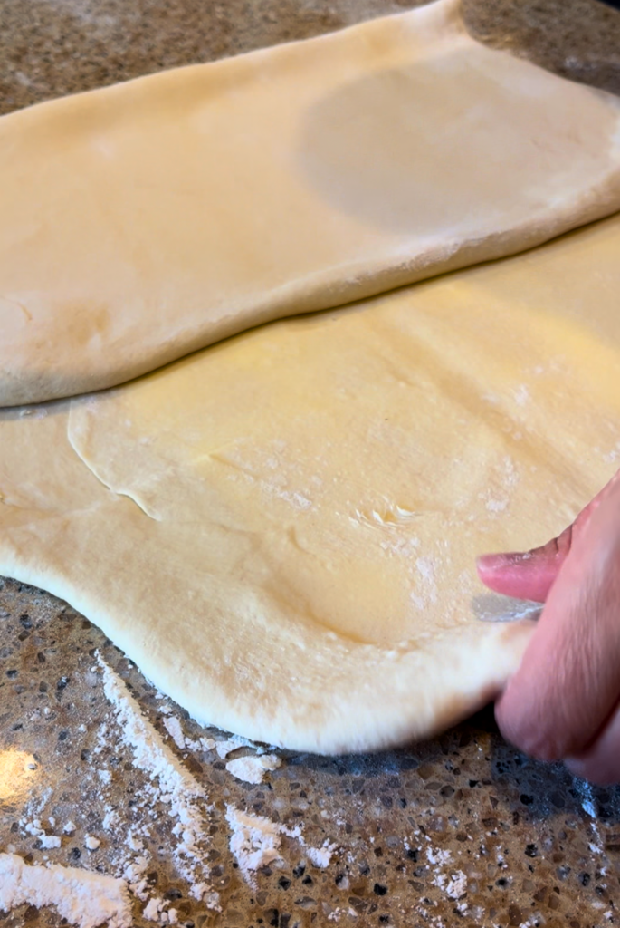 woman folding croissant dough on a brown countertop