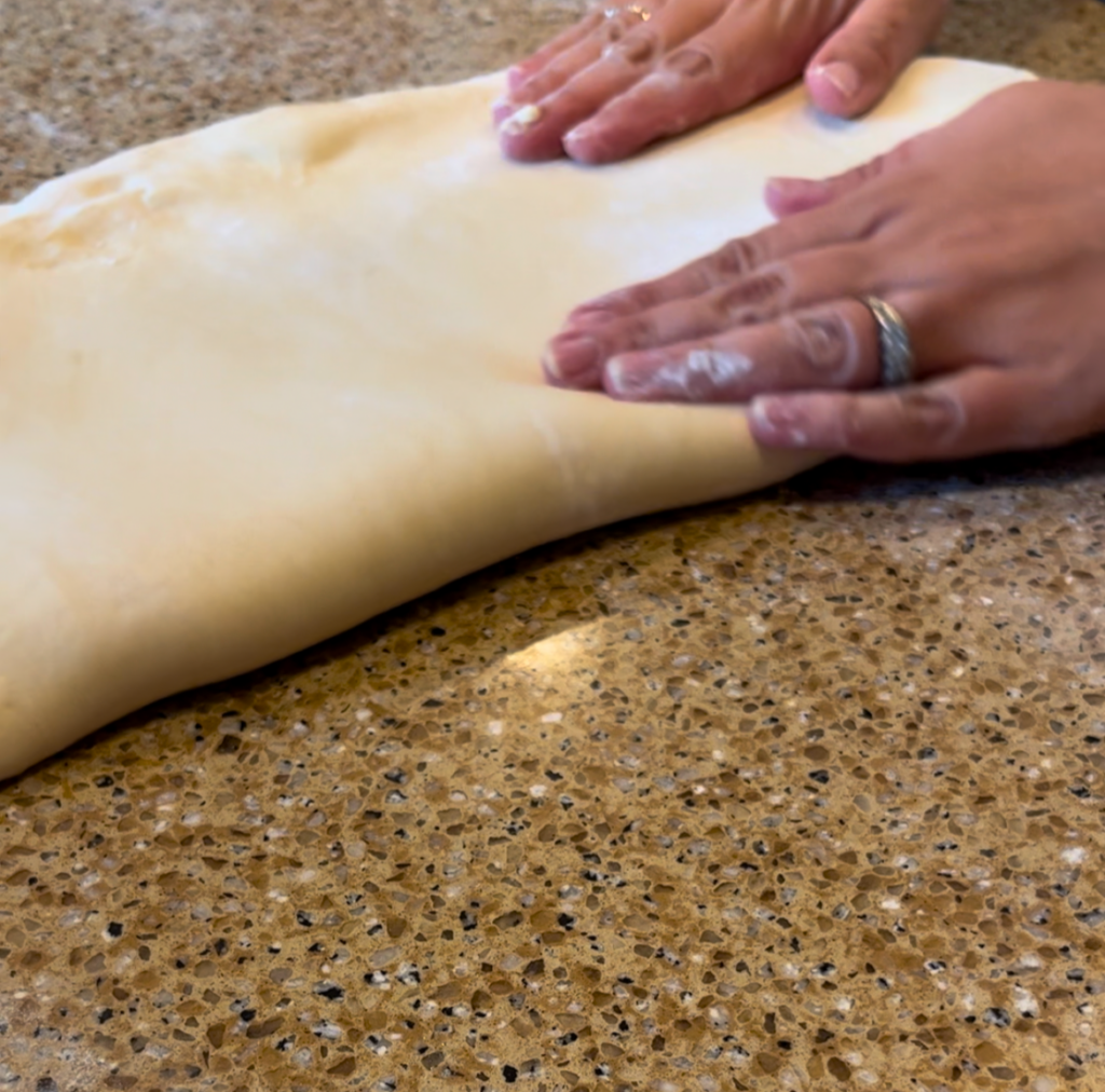 woman folding croissant dough on a brown countertop