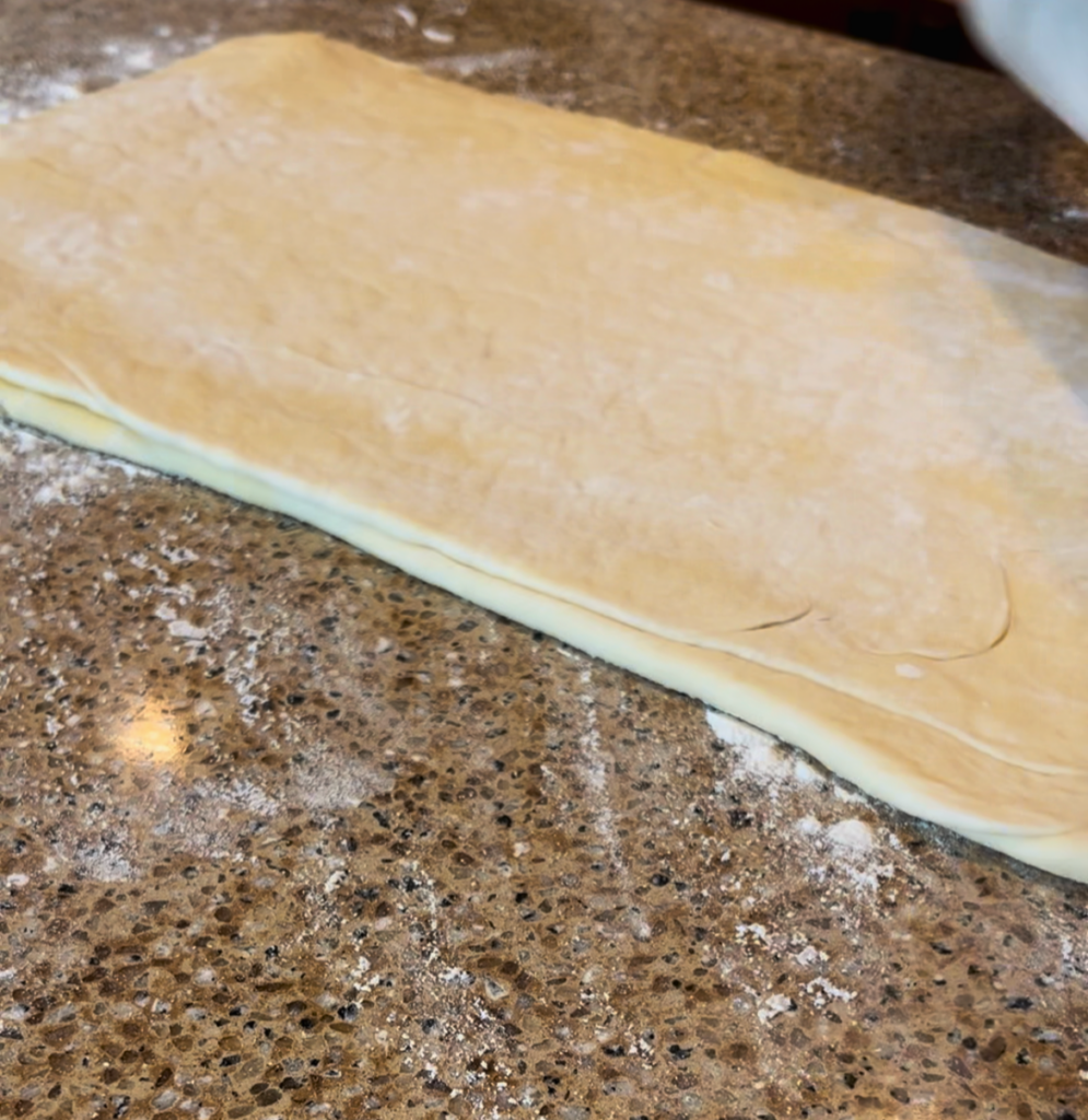 rolling out croissant dough on a brown countertop