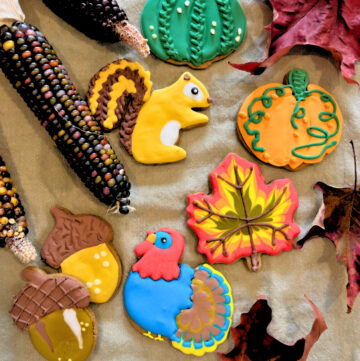 Royal Icing Fall themed sugar cookies surrounded by maple leaves and Indian corn.