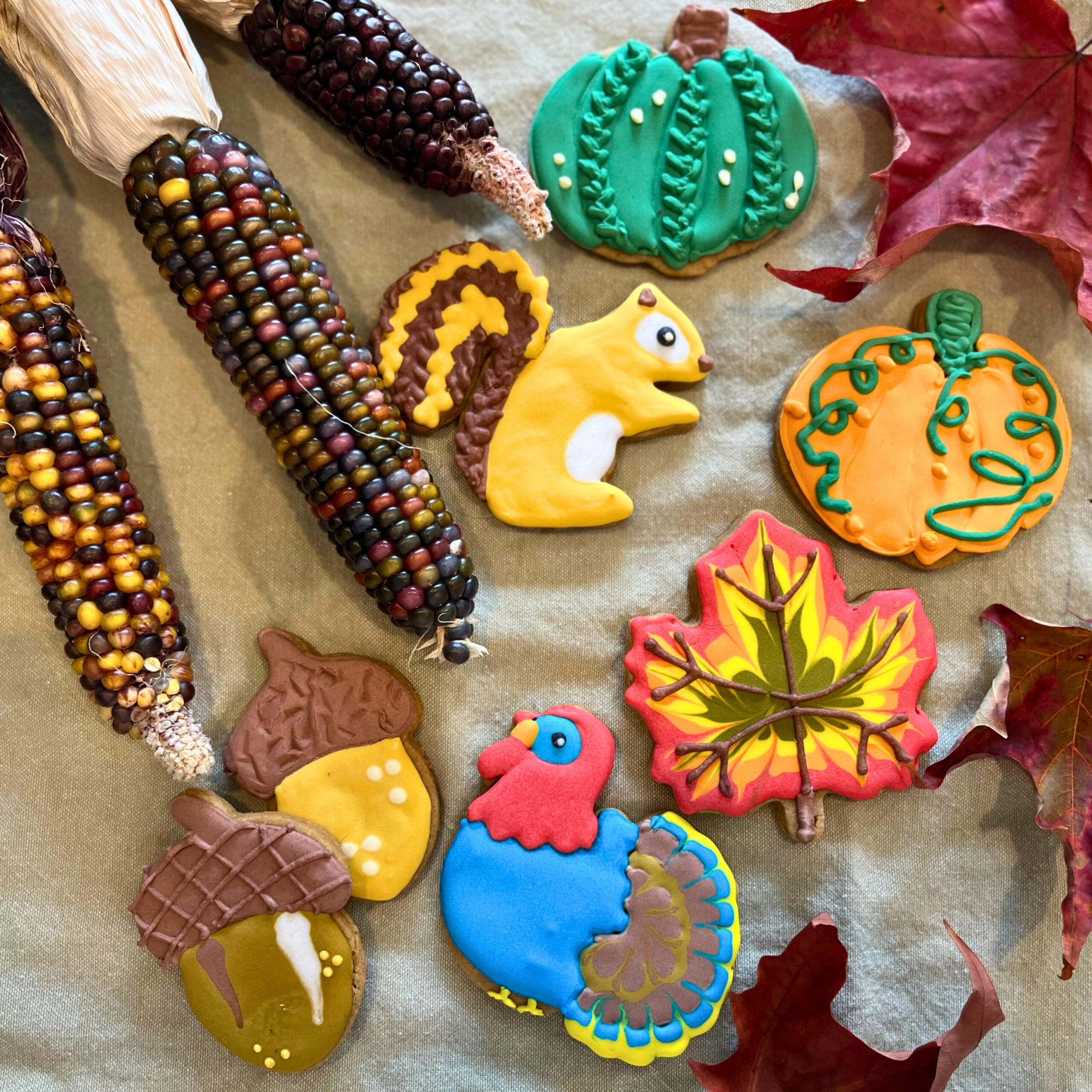 Decorated fall themed sugar cookies surrounded by maple leaves and Indian corn